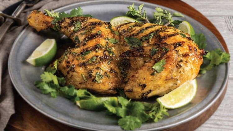 A half Bell & Evans chicken shown cooking using their Grilled Mojo Chicken, plated and ready to be enjoyed.