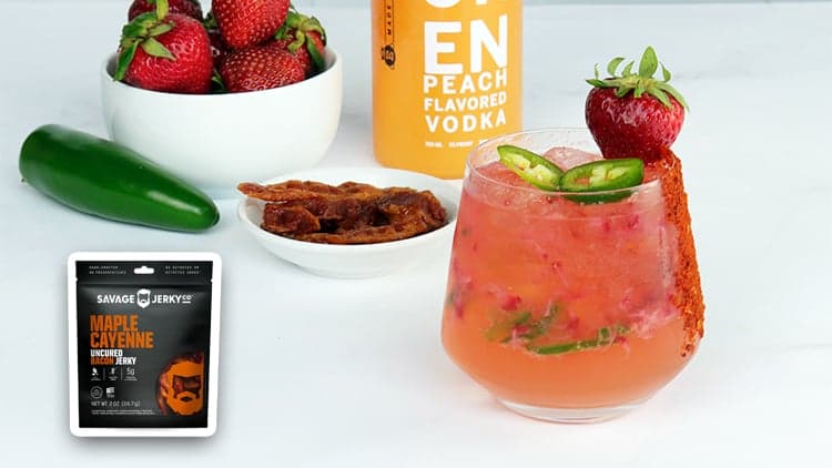 A glass of Peach Strawberry Jalapeño Smash in front of the ingredients used to make it.