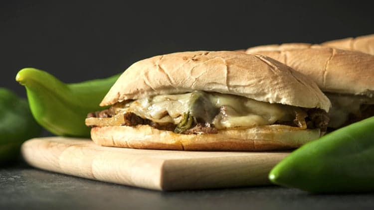 A Hatch Chile Philly Cheesesteak on a board, surrounded by the ingredients used to make it, ready to enjoyed.