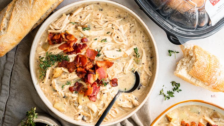 A bowl of Creamy Chicken Chowder with a spoon sitting on it, surrounded by some of the ingredients and ready to be enjoyed.