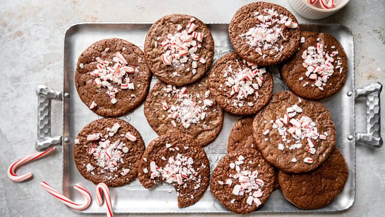 Peppermint Brownie Cookies shown sitting on a baking tray after having cooled, surrounded by mini candy canes.